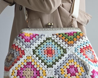Puede incluir: Un bolso de ganchillo hecho con cuadrados de la abuela multicolores en tonos rosa, amarillo, verde, azul y blanco. El bolso cuenta con un marco metálico de cierre a presión con un patrón grabado y una correa de hombro ancha de tela color crema.