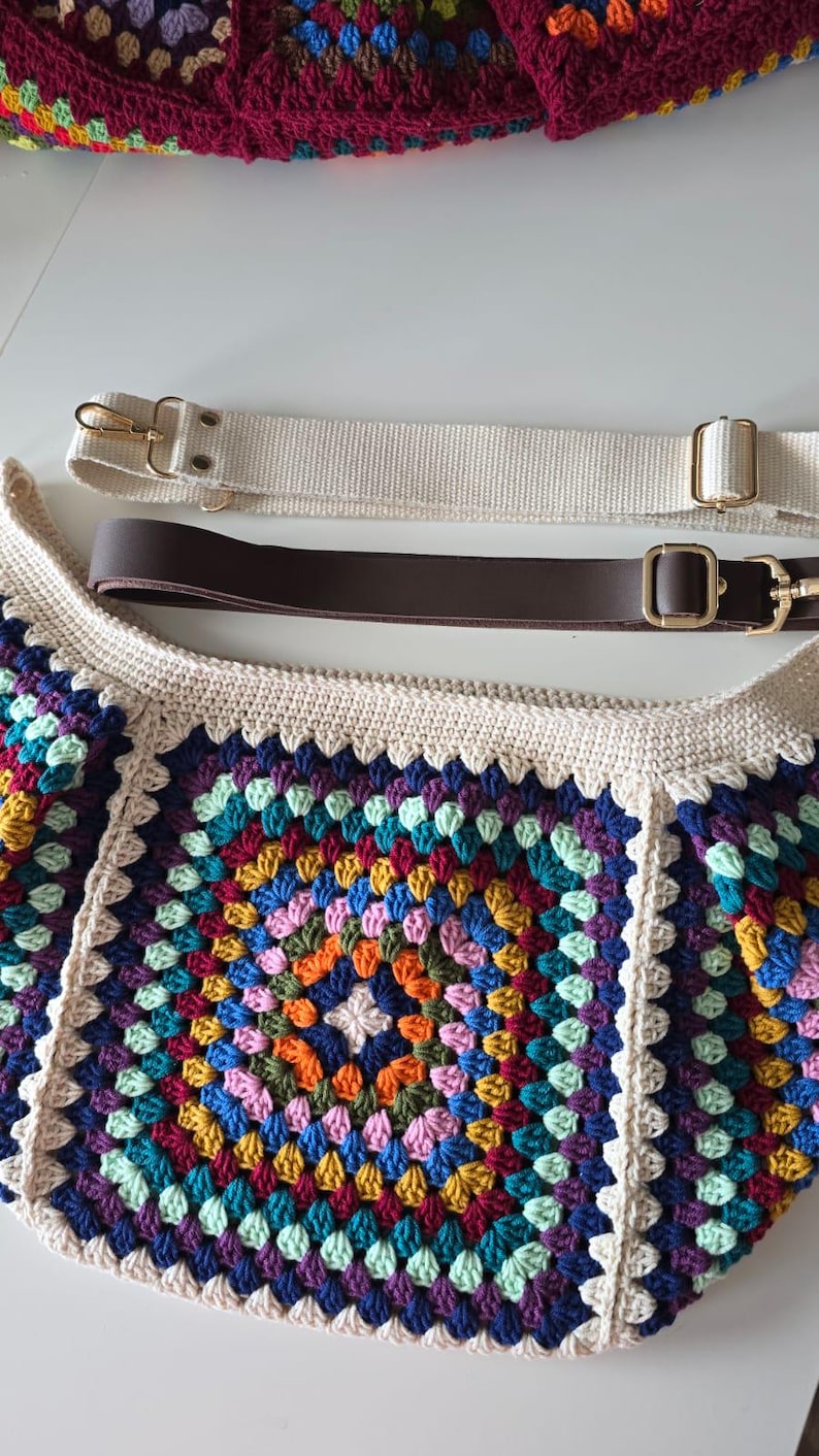 May include: A crocheted bag with a colorful granny square pattern. The bag has two straps, one brown leather and one white canvas.