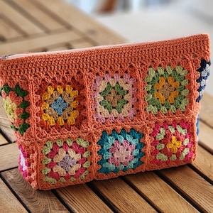 Crochet zipper pouch clutch in bright granny-square panels with orange border; a colorful makeup bag.