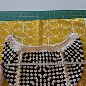 May include: A black and white crocheted tote bag with a round bottom and two gold metal handles. The bag is 28 inches wide.