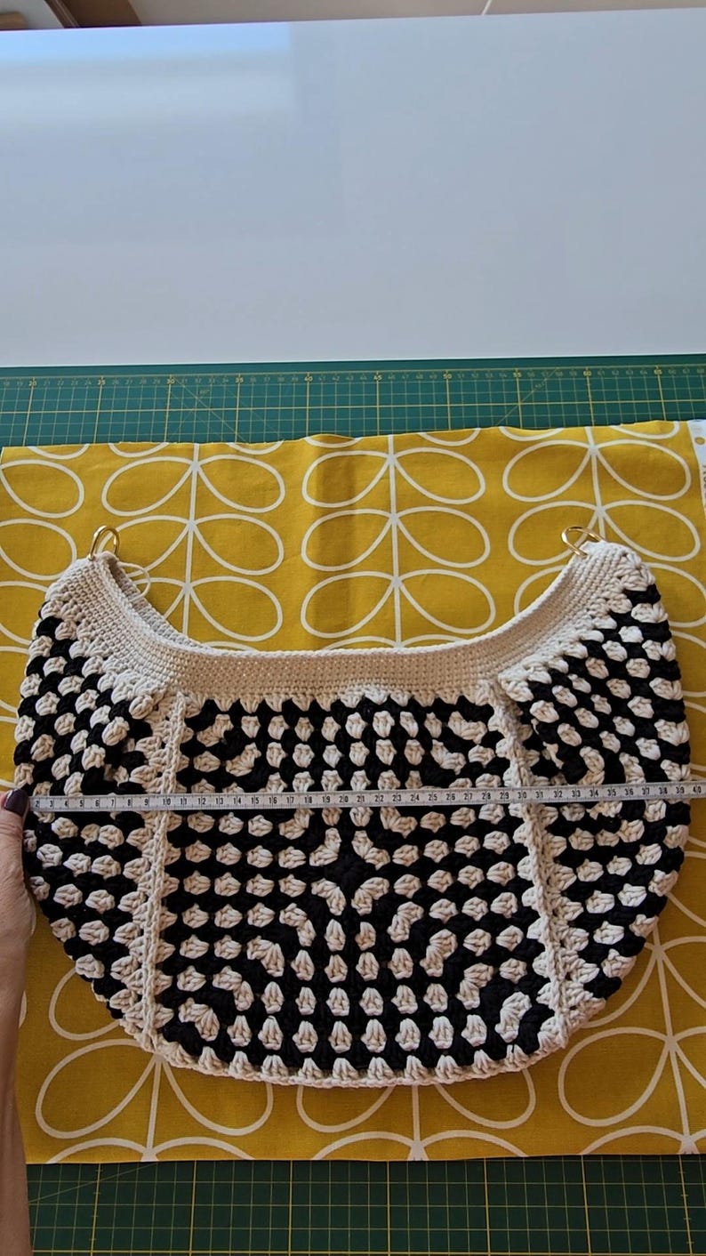 May include: A black and white crocheted tote bag with a round bottom and two gold metal handles. The bag is 28 inches wide.