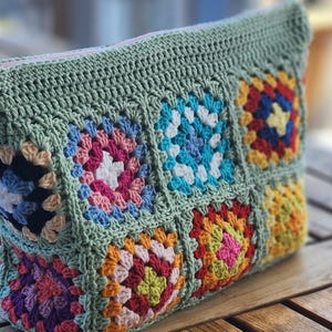 Crochet zipper pouch clutch with green border and multicolor granny square pouch design; pink zipper, ideal for makeup bag.