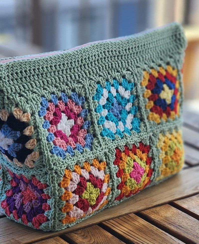 Crochet zipper pouch clutch with green border and multicolor granny square pouch design; pink zipper, ideal for makeup bag.