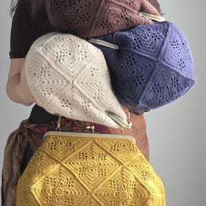 May include: A collection of handmade crochet bags in various colors. The image features a mustard yellow, cream, periwinkle, and brown bag. Each bag has a unique floral pattern and a metal clasp. The bags are a mix of clutch and shoulder bag styles.