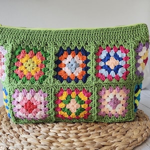 Crochet zipper pouch clutch bag with granny square patchwork in bright colors, green edging, top zipper, on a woven mat.