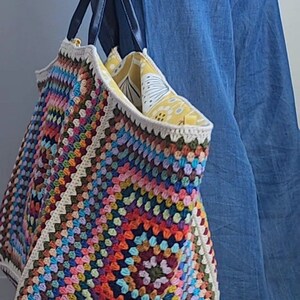 May include: A large, colorful crochet tote bag with a white lining and black handles. The bag is filled with a yellow and white patterned fabric.