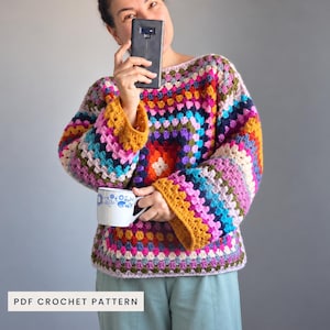 Puede incluir: Un suéter de ganchillo de manga larga con un vibrante patrón de cuadrados de la abuela multicolor en tonos amarillo mostaza, rosa brillante, azul cerceta, azul marino y blanco. La prenda tiene un corte holgado con puños acampanados y el texto PDF CROCHET PATTERN.