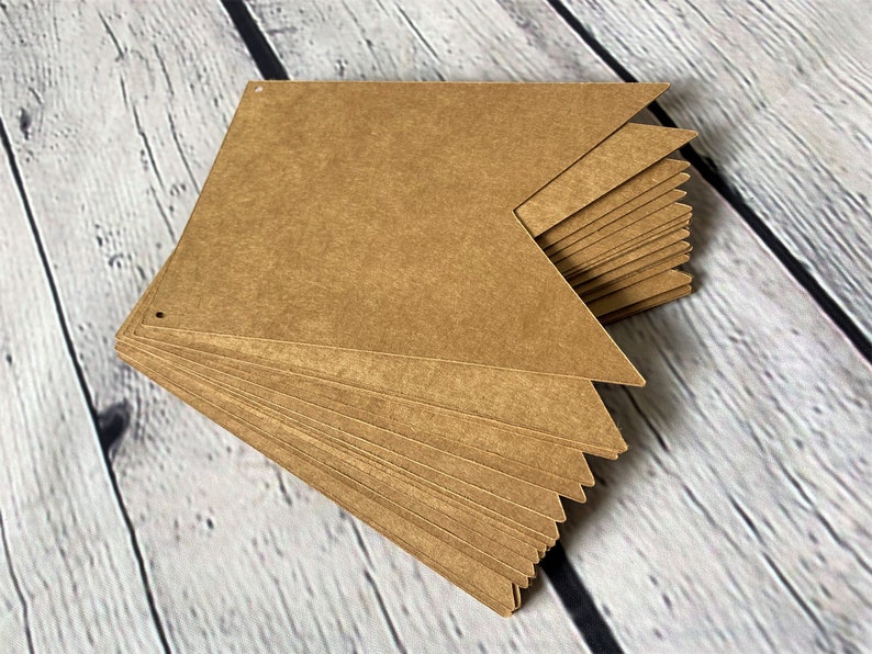 Puede incluir: Una pila de banderas de papel marr&oacute;n con agujeros perforados en las esquinas superiores. Las banderas est&aacute;n dispuestas en forma triangular.