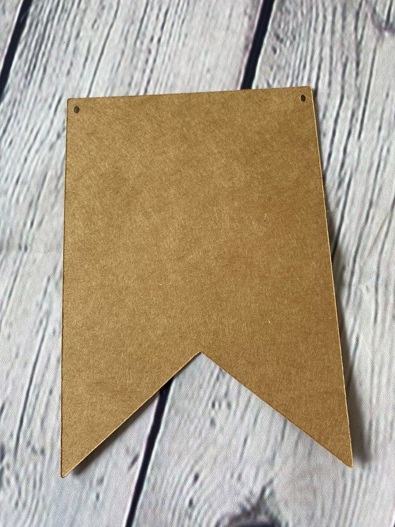 Puede incluir: Una pancarta de papel marr&oacute;n en forma de bander&iacute;n con dos agujeros perforados en la parte superior.