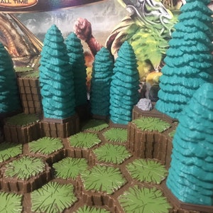 May include: A set of teal green plastic miniature trees on a brown hexagonal base with green grass. The trees are arranged in a cluster on a brown surface.