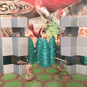 May include: Two gray, modular, multi-level, 3D printed buildings with a gray, textured surface. The buildings are on a hexagonal tile game board with green and brown accents.  The buildings are surrounded by blue and green trees.