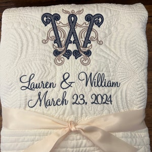 May include: A white quilted throw blanket with a navy blue and brown embroidered monogram "W" and the text "Lauren & William March 23, 2024". The blanket is tied with a cream-colored satin ribbon.