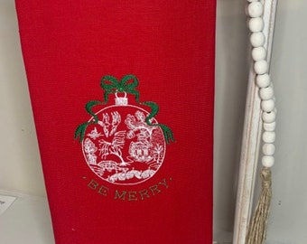 May include: Red kitchen towel with a white embroidered ornament and the text "Be Merry".