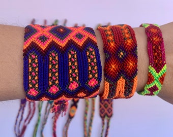 May include: A set of colorful friendship bracelets with geometric patterns in shades of orange, red, green, blue, and pink. The bracelets are made with woven thread and have tassels.