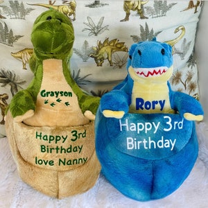 May include: Two plush dinosaur toys, one green and one blue, with personalized embroidery. The green dinosaur says "Grayson Happy 3rd Birthday love Nanny" and the blue dinosaur says "Rory Happy 3rd Birthday".