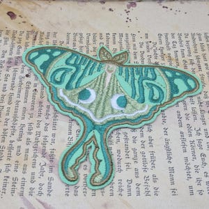 May include: Embroidered moth patch in shades of teal, green, and gold. The detailed design features a Luna moth with intricate wing patterns and a delicate, nature-inspired aesthetic. Perfect for adding to clothing or accessories.