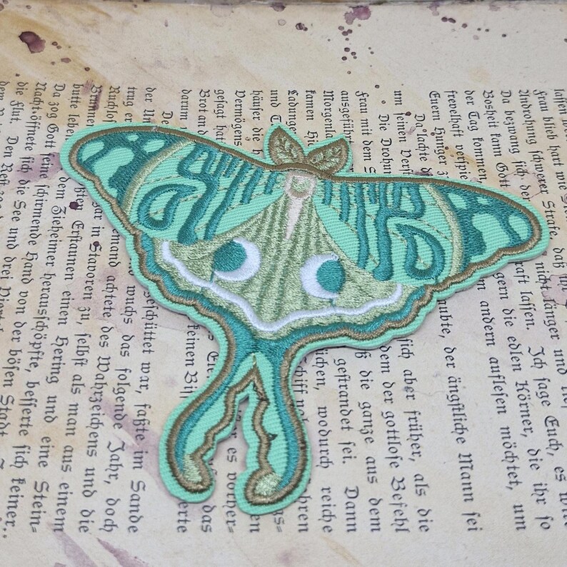 May include: Embroidered moth patch in shades of teal, green, and gold. The detailed design features a Luna moth with intricate wing patterns and a delicate, nature-inspired aesthetic. Perfect for adding to clothing or accessories.
