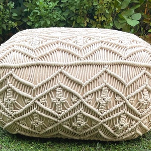 May include: A cream-colored, round, woven ottoman with a geometric pattern. The ottoman is made of thick rope and has a soft, plush texture.