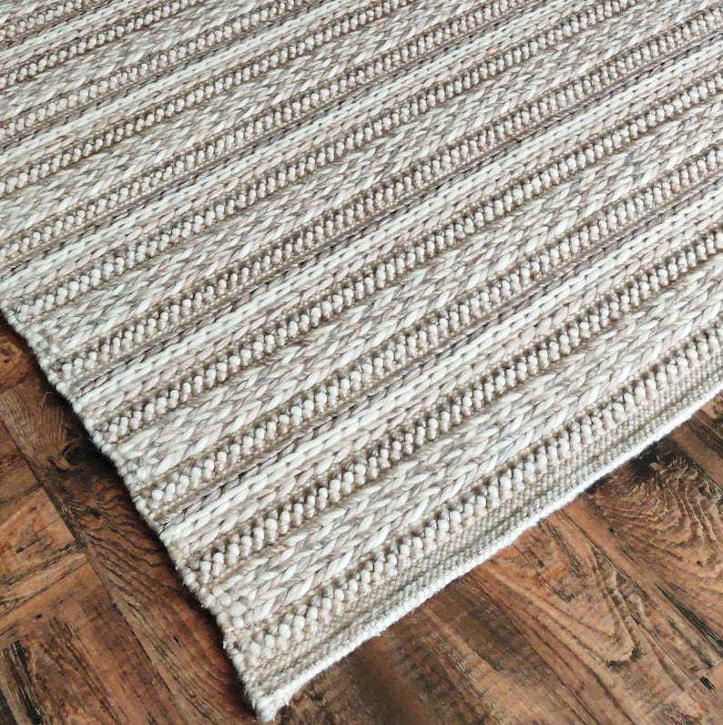 May include: A beige and white striped rug with a woven texture. The rug has a subtle sheen and a slightly raised surface.