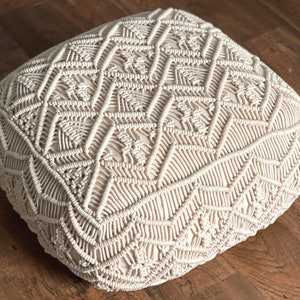May include: A cream-colored, round, woven floor cushion with a geometric pattern. The cushion is made of thick, knotted rope and has a soft, textured surface.