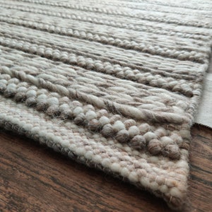 May include: Close-up of a beige and white woven rug with a textured surface. The rug has a label that says "LOOMINARE" in black text.