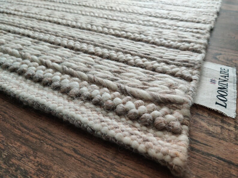May include: Close-up of a beige and white woven rug with a textured surface. The rug has a label that says "LOOMINARE" in black text.