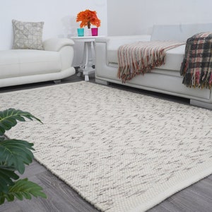 May include: A white, fluffy rug with a subtle gray pattern. The rug is laid out on a wooden floor in a living room setting with white furniture.