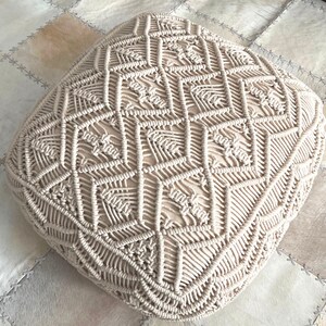 May include: A cream-colored, square-shaped, woven floor cushion with a geometric pattern.