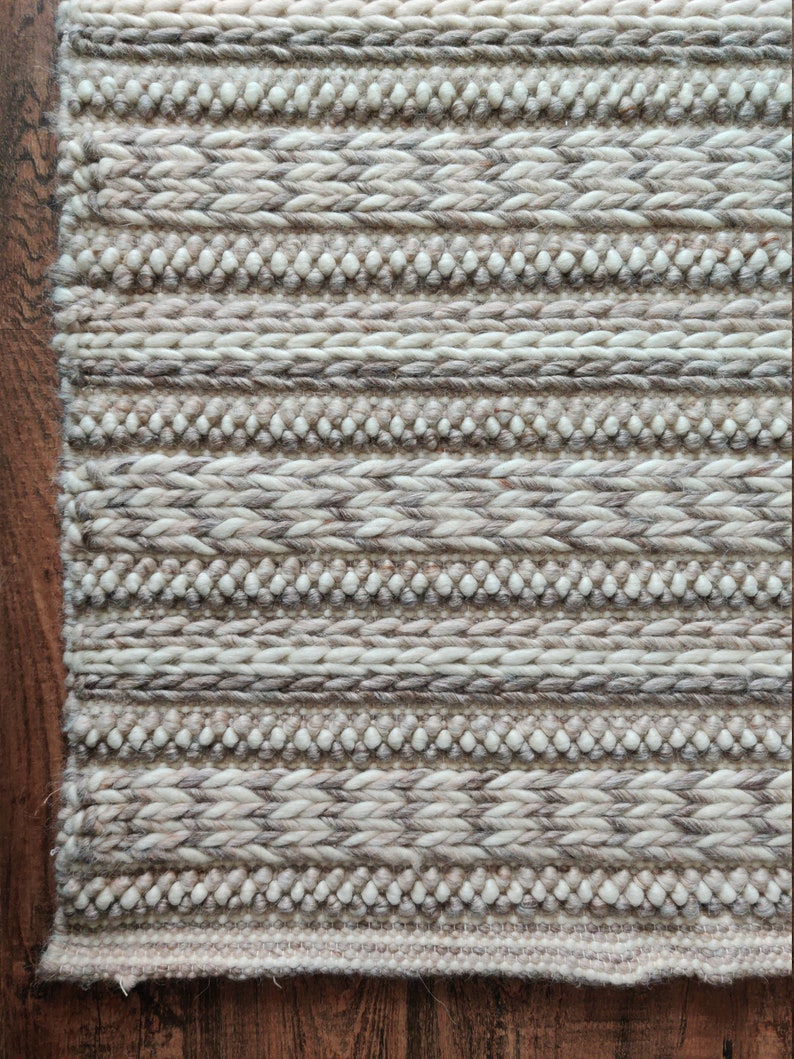 May include: A close-up of a woven rug with a cream and brown striped pattern. The rug has a textured surface and is made of natural fibers.