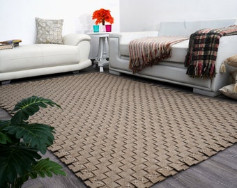 May include: A light brown woven rug with a geometric pattern. The rug is placed in a living room setting with white couches and a small table with a potted plant.
