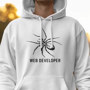 May include: White hoodie featuring a black spider illustration and the words "WEB DEVELOPER". The hoodie includes a hood with a drawstring and a front pocket. The design is centrally placed.