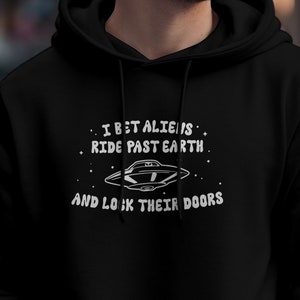 May include: Black hoodie with a white graphic print of a UFO and the text "I bet aliens ride past earth and look their doors".