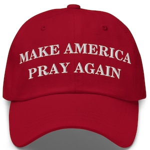 May include: A red baseball cap with the embroidered text "MAKE AMERICA PRAY AGAIN" in white. The cap has a curved brim and a rounded top, typical of a baseball cap design.