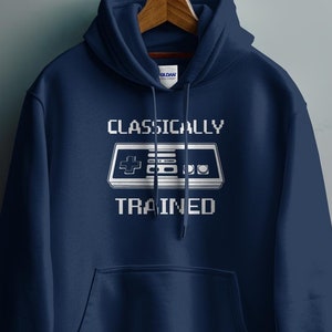 May include: A navy blue hoodie with a white graphic of a classic video game controller and the text "CLASSICALLY TRAINED".