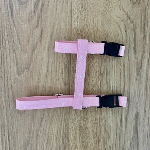 Puede incluir: Arn&eacute;s ajustable para perro de color rosa con estampado floral blanco y hebillas de pl&aacute;stico negras.