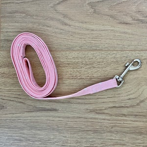Puede incluir: Una correa de perro rosa con un clip plateado. La correa est&aacute; enrollada y el clip est&aacute; unido al extremo de la correa.