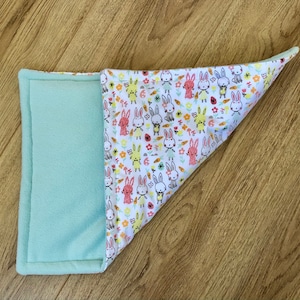 May include: A light blue fleece-lined baby blanket with a white fabric side featuring a repeating pattern of colorful bunnies and carrots.