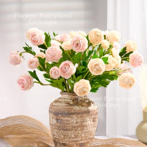 Peut inclure: Un bouquet de renoncules rose p&acirc;le dispos&eacute; dans un vase en c&eacute;ramique brun rustique. Les fleurs sont en pleine floraison et ont une apparence d&eacute;licate et f&eacute;minine.