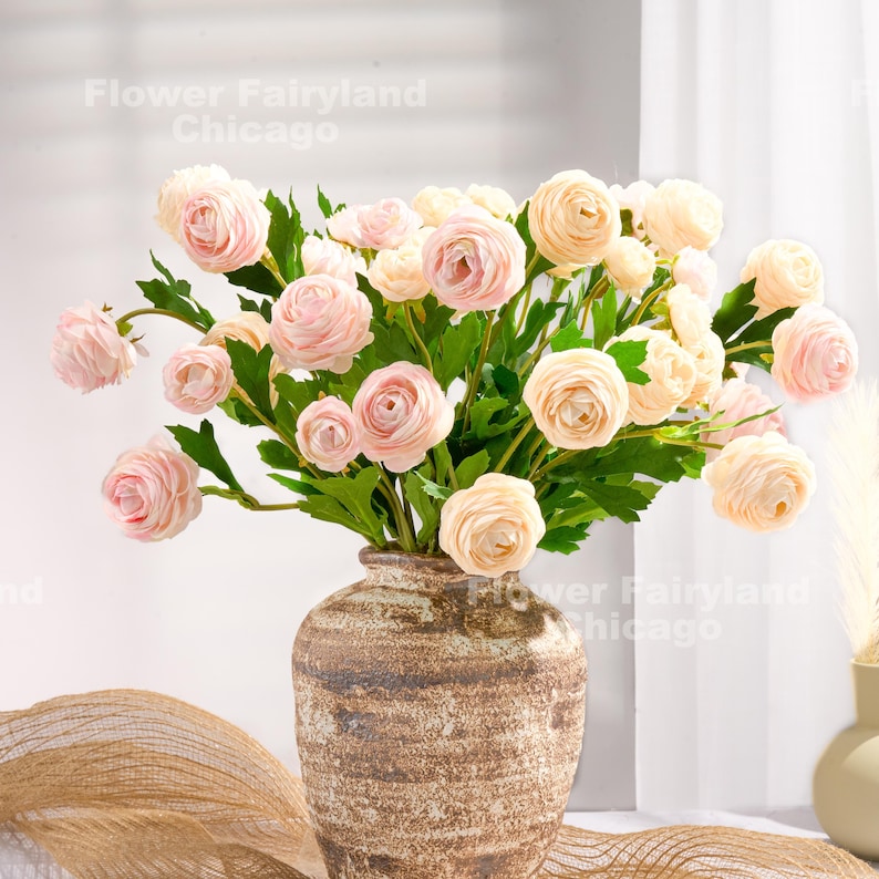 Peut inclure: Un bouquet de renoncules rose p&acirc;le dispos&eacute; dans un vase en c&eacute;ramique brun rustique. Les fleurs sont en pleine floraison et ont une apparence d&eacute;licate et f&eacute;minine.