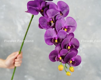 Puede incluir: Un ramo de flores de orquídea de seda púrpura con capullos amarillos en un tallo verde.