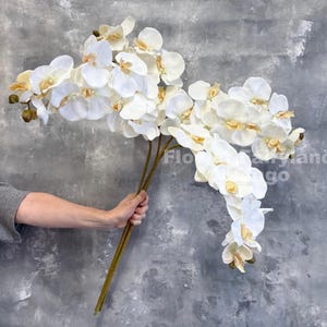 Op de afbeelding: Een boeket witte zijden orchideeën met bruine stelen. De orchideeën hebben een delicate, realistische uitstraling.