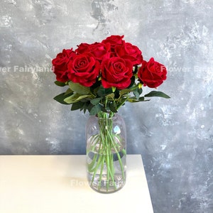 May include: A bouquet of red roses in a clear glass vase. The roses are arranged in a cluster and have green stems and leaves.