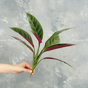 以下が含まれることがあります： 緑と赤の人工の葉の束。裏側はワインレッド。葉にはストライプ模様が入っている。