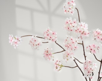May include: Artificial cherry blossom branches with clusters of delicate, light pink flowers and dark brown stems. The blossoms have a soft, layered appearance, creating a natural and elegant aesthetic. Ideal for home decor or floral arrangements.