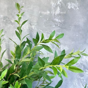 May include: A bunch of green artificial leaves with a light gray background. The leaves are arranged in a cluster and have a natural, realistic appearance.