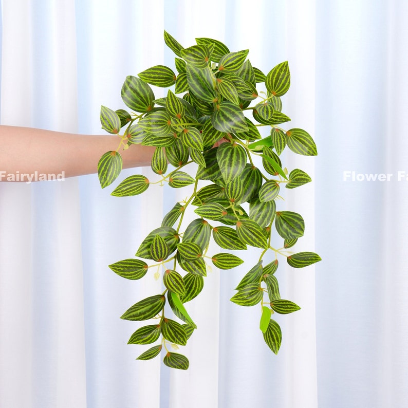 May include: A long, green artificial plant with striped leaves. The plant is hanging down and has a natural, realistic look.