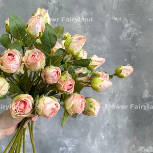 May include: A bouquet of pink artificial roses with green leaves. The roses are arranged in a cluster and have a soft, delicate appearance.