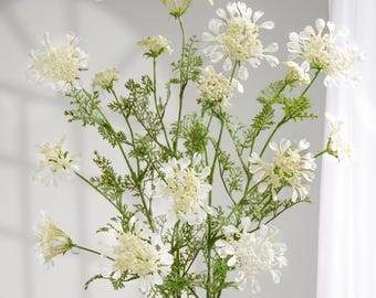 May include: A bouquet of white artificial flowers with green stems and leaves in a white vase. The flowers have a delicate, layered appearance. The text "Flower Fairyland Chicago" is in the upper left corner.