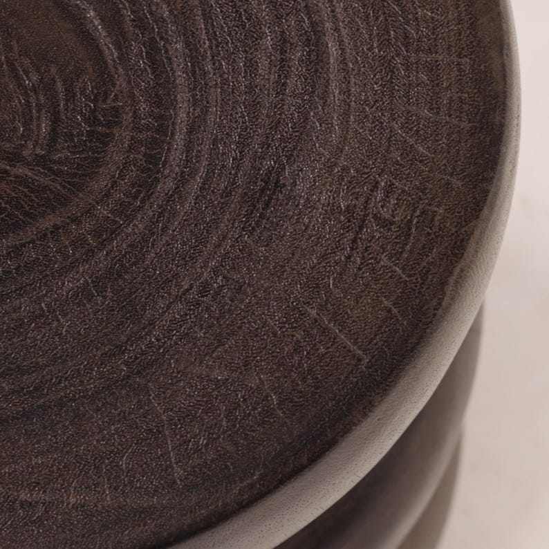 May include: A set of three dark brown wooden nesting tables with a circular top. The top table has a wood grain pattern and the words "Made in Italy" inscribed on the surface.