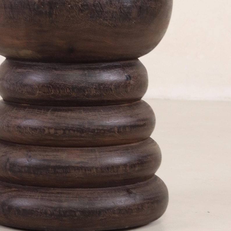 May include: A dark brown wooden pedestal with a rounded top and a series of stacked, rounded rings.